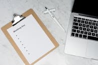 Flat lay of a wedding planning setting with clipboard, laptop, and pen.